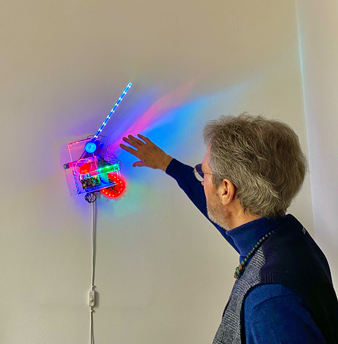 Ein älterer Mann zeigt auf ein Medienkunstwerk an der Wand